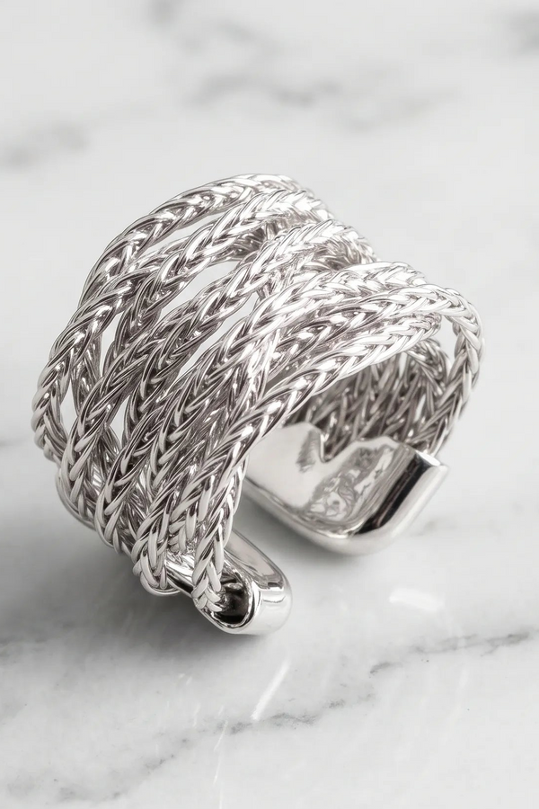 A wide silver-toned braided ring with an open back, photographed on a light marble surface.