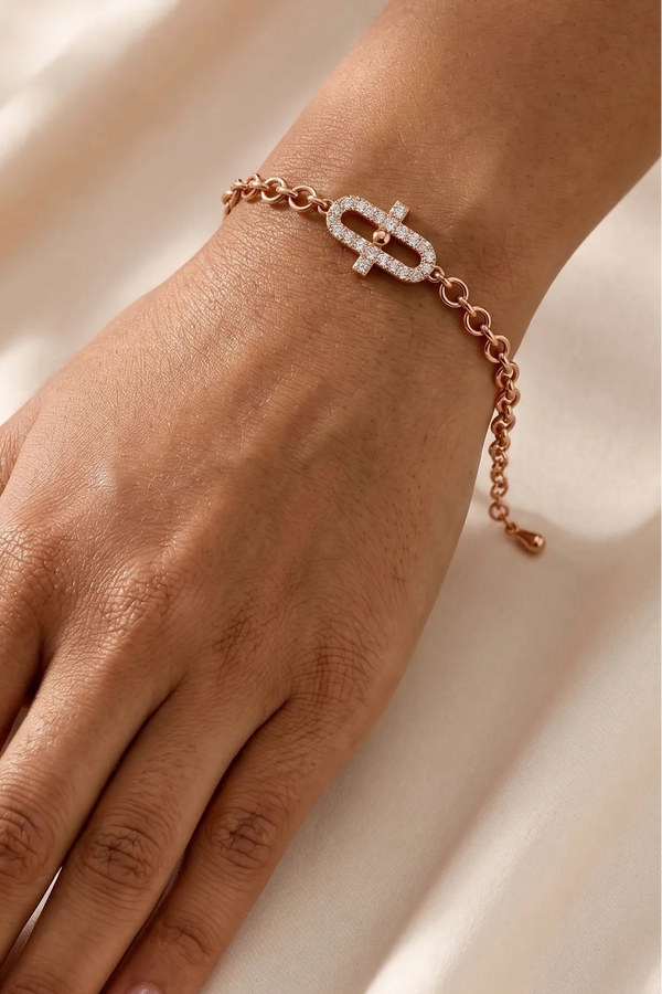 A close-up of a person's hand wearing a delicate rose gold chain bracelet with a geometric link design set with clear stones, resting on a soft, draped cream fabric background.