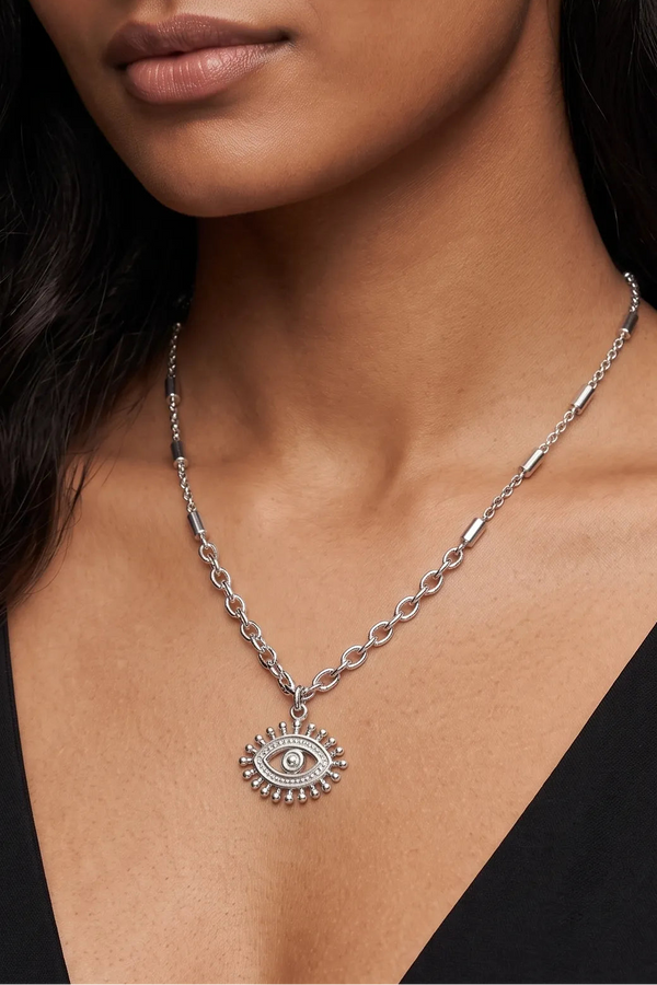 A close-up of a model wearing a silver chain necklace with a detailed evil eye pendant.