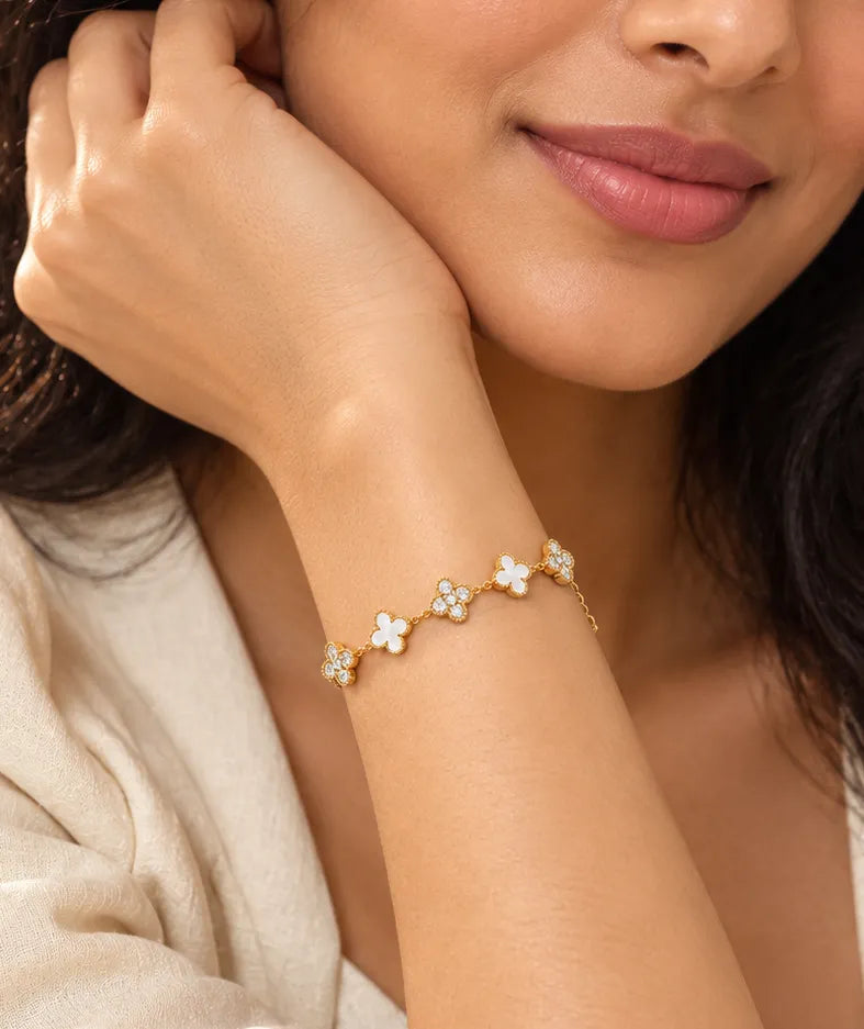 A close-up lifestyle shot of a woman wearing a delicate gold chain bracelet adorned with small white flower charms, each embellished with tiny clear stones.