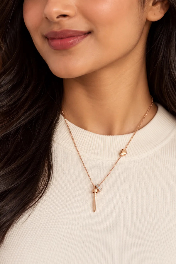 A close-up of a woman wearing a delicate rose gold necklace with a small key and heart pendant, paired with a cream-colored ribbed sweater.