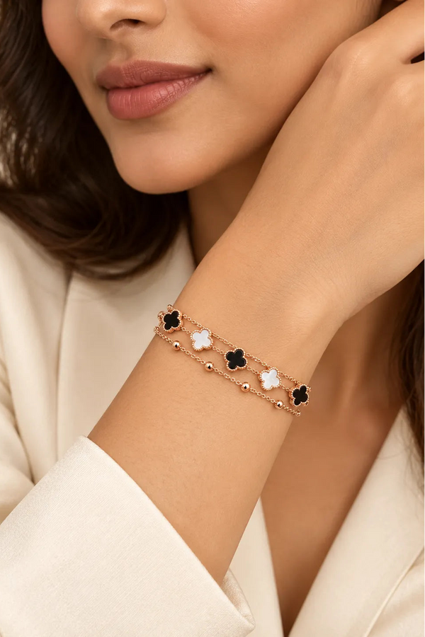 A close-up of a woman wearing a delicate rose gold chain bracelet with alternating black and white clover motifs on her wrist.