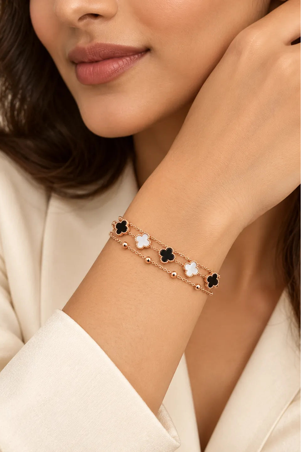 A close-up of a woman wearing a delicate rose gold chain bracelet with alternating black and white clover motifs on her wrist.